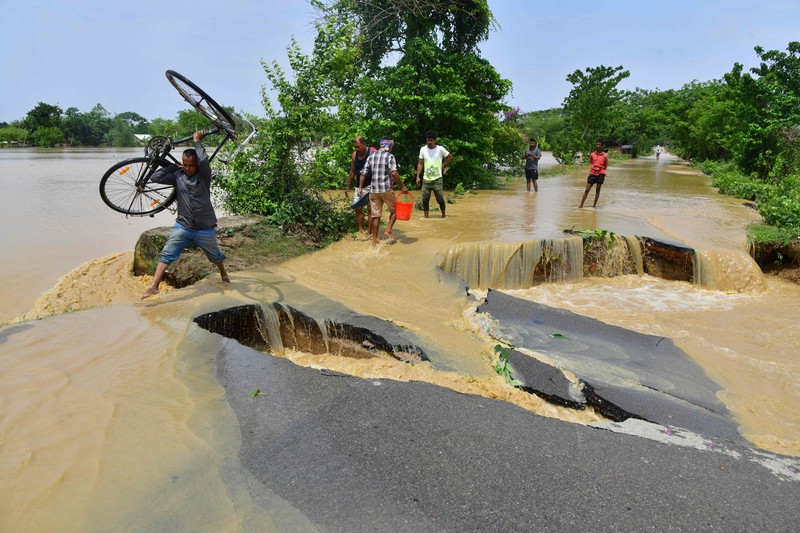 Anak-anak menaiki rakit bambu melewati daerah banjir setelah hujan lebat di distrik Morigaon, negara bagian Assam, India, Minggu (22/5/2022). Banjir adalah ancaman biasa bagi jutaan orang di dataran rendah Bangladesh dan tetangga timur laut India, tetapi banyak ahli mengatakan bahwa perubahan iklim meningkatkan frekuensi, keganasan dan ketidakpastian. (Photo by BIJU BORO/AFP via Getty Images)