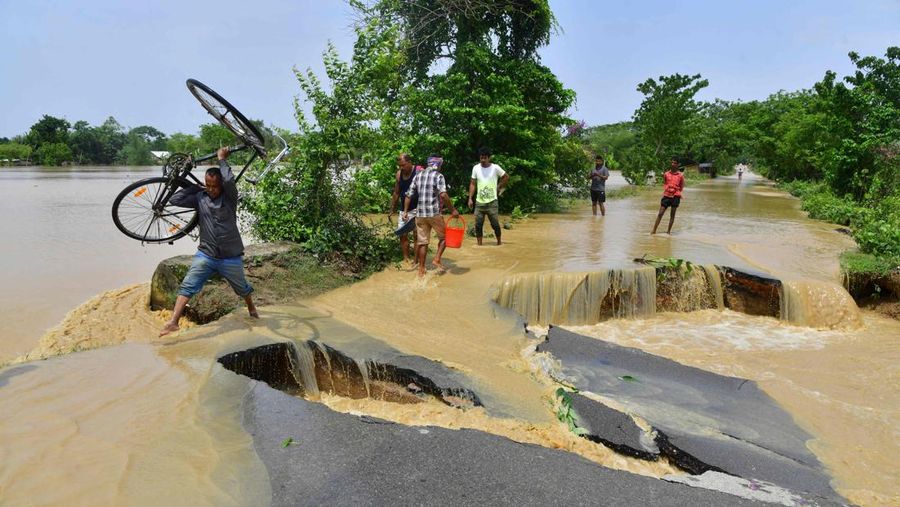 Anak-anak menaiki rakit bambu melewati daerah banjir setelah hujan lebat di distrik Morigaon, negara bagian Assam, India, Minggu (22/5/2022). Banjir adalah ancaman biasa bagi jutaan orang di dataran rendah Bangladesh dan tetangga timur laut India, tetapi banyak ahli mengatakan bahwa perubahan iklim meningkatkan frekuensi, keganasan dan ketidakpastian. (Photo by BIJU BORO/AFP via Getty Images)