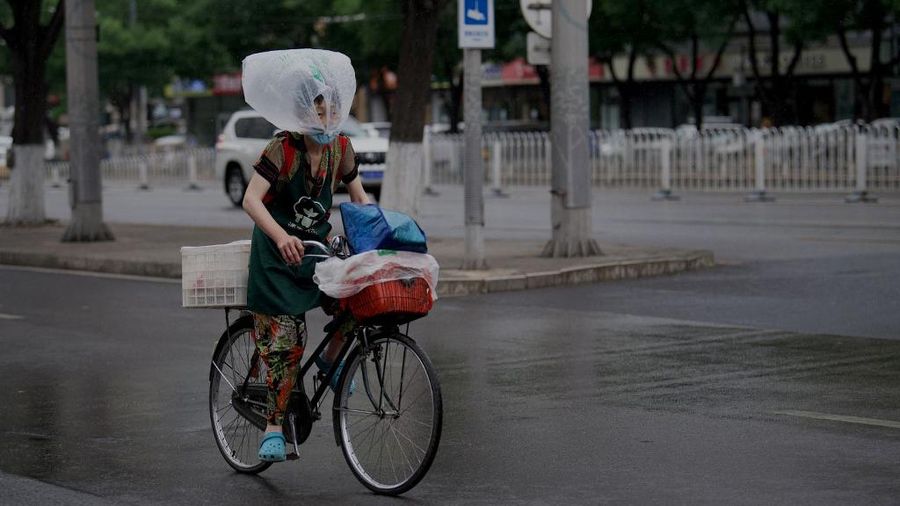 Seorang wanita menggunakan kantong plastik sebagai penutup hujan saat dia bersepeda di sepanjang jalan di Beijing. (AFP/NOEL CELIS)