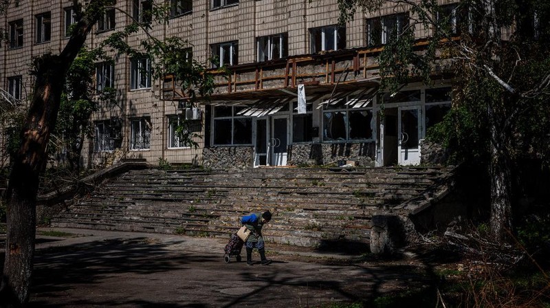 Seorang gadis berjalan di depan gedung apartemen yang rusak setelah serangan Rusia ke Ukraina di kota Slovyansk di wilayah Donbas, Ukraina timur, Selasa (31/5/2022). (Photo by ARIS MESSINIS / AFP)