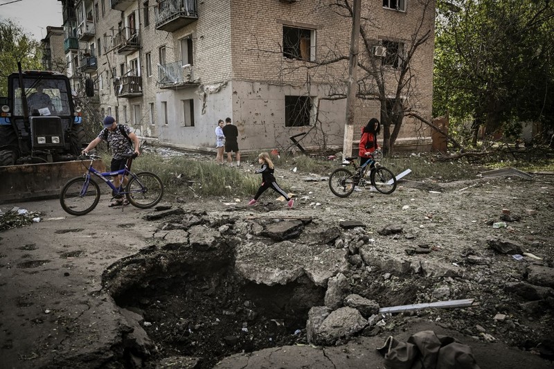 Seorang gadis berjalan di depan gedung apartemen yang rusak setelah serangan Rusia ke Ukraina di kota Slovyansk di wilayah Donbas, Ukraina timur, Selasa (31/5/2022). (Photo by ARIS MESSINIS / AFP)