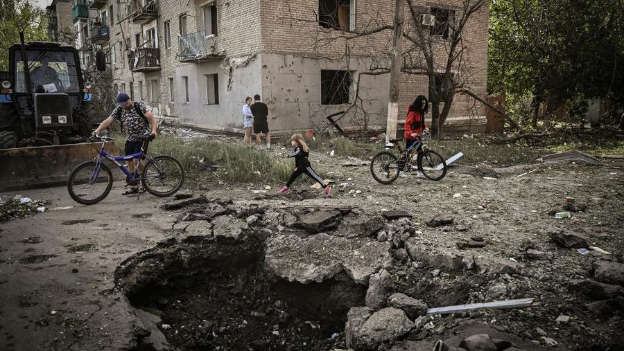 Seorang gadis berjalan di depan gedung apartemen yang rusak setelah serangan Rusia ke Ukraina di kota Slovyansk di wilayah Donbas, Ukraina timur, Selasa (31/5/2022). (Photo by ARIS MESSINIS / AFP)