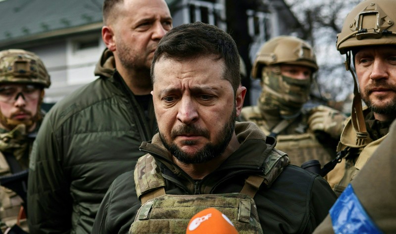TOPSHOT - People standing near a Ukrainian national flag watch as dark smoke billows following an air strike in the western Ukrainian city of Lviv, on March 26, 2022. - At least five people wounded in two strikes on Lviv, the regional governor said, in a rare attack on a city that has escaped serious fighting since Russian troops invaded last month. (Photo by Aleksey Filippov / AFP) (Photo by ALEKSEY FILIPPOV/AFP via Getty Images)