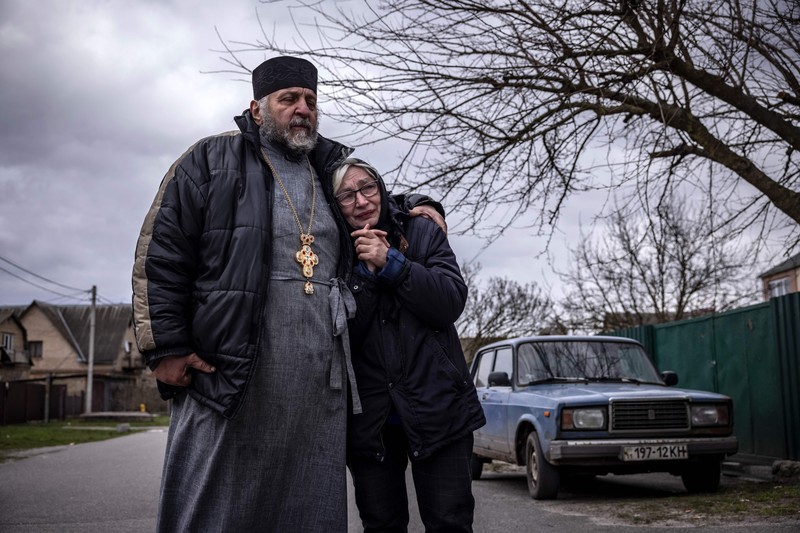 TOPSHOT - People standing near a Ukrainian national flag watch as dark smoke billows following an air strike in the western Ukrainian city of Lviv, on March 26, 2022. - At least five people wounded in two strikes on Lviv, the regional governor said, in a rare attack on a city that has escaped serious fighting since Russian troops invaded last month. (Photo by Aleksey Filippov / AFP) (Photo by ALEKSEY FILIPPOV/AFP via Getty Images)