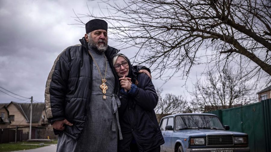 TOPSHOT - People standing near a Ukrainian national flag watch as dark smoke billows following an air strike in the western Ukrainian city of Lviv, on March 26, 2022. - At least five people wounded in two strikes on Lviv, the regional governor said, in a rare attack on a city that has escaped serious fighting since Russian troops invaded last month. (Photo by Aleksey Filippov / AFP) (Photo by ALEKSEY FILIPPOV/AFP via Getty Images)