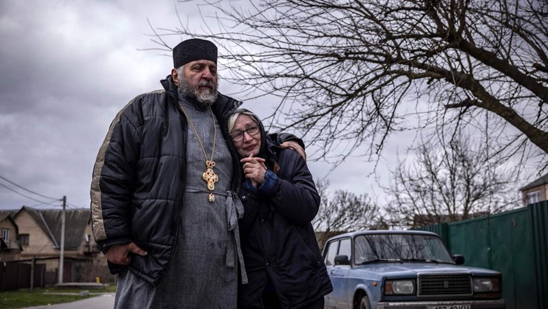 TOPSHOT - People standing near a Ukrainian national flag watch as dark smoke billows following an air strike in the western Ukrainian city of Lviv, on March 26, 2022. - At least five people wounded in two strikes on Lviv, the regional governor said, in a rare attack on a city that has escaped serious fighting since Russian troops invaded last month. (Photo by Aleksey Filippov / AFP) (Photo by ALEKSEY FILIPPOV/AFP via Getty Images)