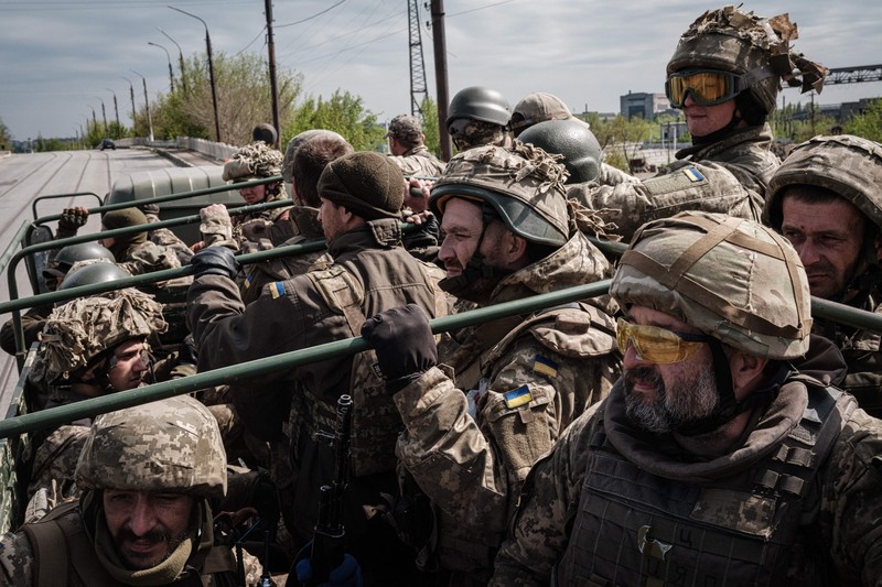 TOPSHOT - People standing near a Ukrainian national flag watch as dark smoke billows following an air strike in the western Ukrainian city of Lviv, on March 26, 2022. - At least five people wounded in two strikes on Lviv, the regional governor said, in a rare attack on a city that has escaped serious fighting since Russian troops invaded last month. (Photo by Aleksey Filippov / AFP) (Photo by ALEKSEY FILIPPOV/AFP via Getty Images)