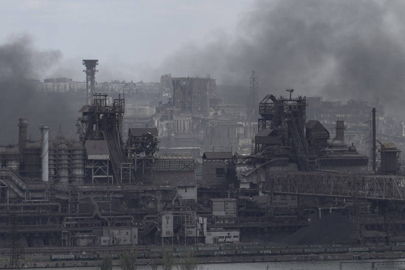 1239523382 TOPSHOT - People standing near a Ukrainian national flag watch as dark smoke billows following an air strike in the western Ukrainian city of Lviv, on March 26, 2022. - At least five people wounded in two strikes on Lviv, the regional governor said, in a rare attack on a city that has escaped serious fighting since Russian troops invaded last month. (Photo by Aleksey Filippov / AFP) (Photo by ALEKSEY FILIPPOV/AFP via Getty Images)