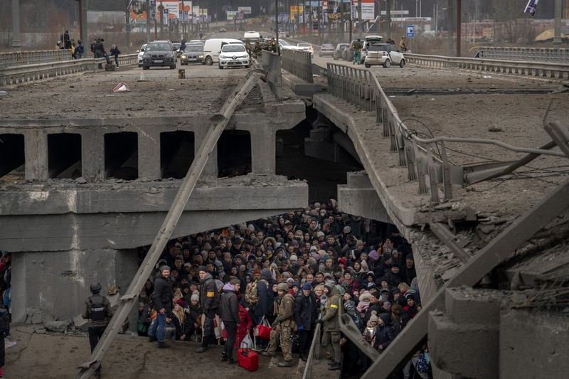 1239523382 TOPSHOT - People standing near a Ukrainian national flag watch as dark smoke billows following an air strike in the western Ukrainian city of Lviv, on March 26, 2022. - At least five people wounded in two strikes on Lviv, the regional governor said, in a rare attack on a city that has escaped serious fighting since Russian troops invaded last month. (Photo by Aleksey Filippov / AFP) (Photo by ALEKSEY FILIPPOV/AFP via Getty Images)