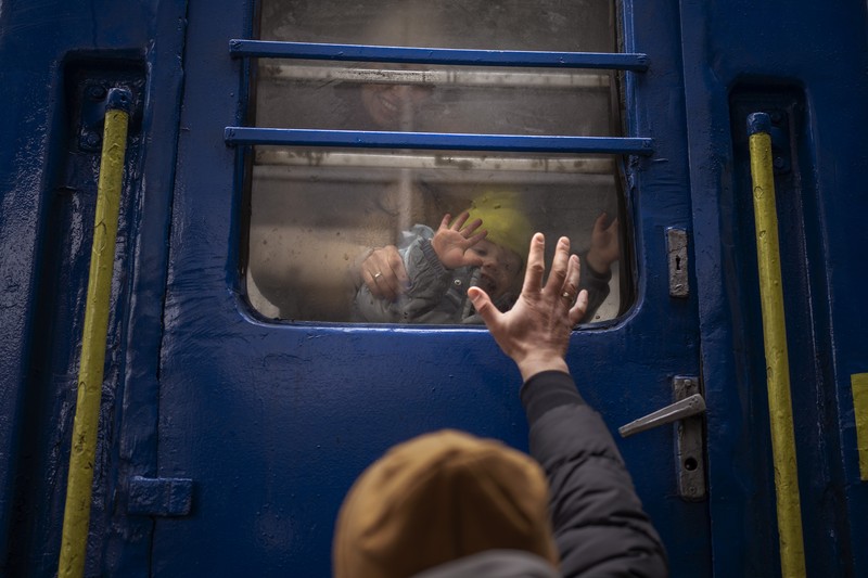 1239523382 TOPSHOT - People standing near a Ukrainian national flag watch as dark smoke billows following an air strike in the western Ukrainian city of Lviv, on March 26, 2022. - At least five people wounded in two strikes on Lviv, the regional governor said, in a rare attack on a city that has escaped serious fighting since Russian troops invaded last month. (Photo by Aleksey Filippov / AFP) (Photo by ALEKSEY FILIPPOV/AFP via Getty Images)