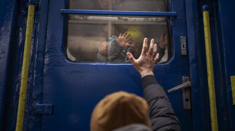TOPSHOT - People standing near a Ukrainian national flag watch as dark smoke billows following an air strike in the western Ukrainian city of Lviv, on March 26, 2022. - At least five people wounded in two strikes on Lviv, the regional governor said, in a rare attack on a city that has escaped serious fighting since Russian troops invaded last month. (Photo by Aleksey Filippov / AFP) (Photo by ALEKSEY FILIPPOV/AFP via Getty Images)
