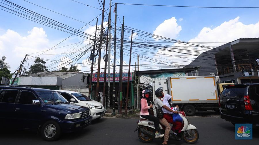Kendaraan melintas di samping kabel yang semrawut di kawasan jalan Raya Pd. Gede, Pinang Ranti, Jakarta Timur, Jumat (3/6/2022). (CNBC Indonesia/ Andrean Kristianto)