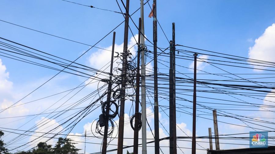 Kendaraan melintas di samping kabel yang semrawut di kawasan jalan Raya Pd. Gede, Pinang Ranti, Jakarta Timur, Jumat (3/6/2022). (CNBC Indonesia/ Andrean Kristianto)