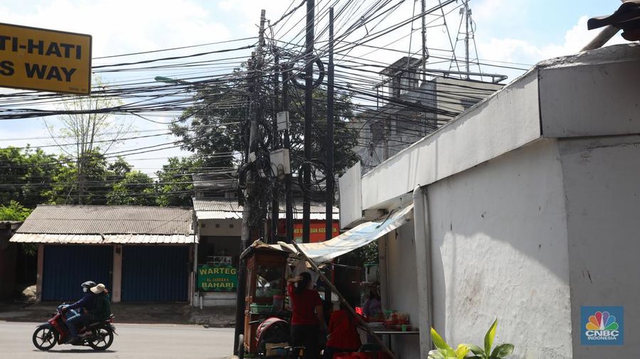 Kendaraan melintas di samping kabel yang semrawut di kawasan jalan Raya Pd. Gede, Pinang Ranti, Jakarta Timur, Jumat (3/6/2022). (CNBC Indonesia/ Andrean Kristianto)