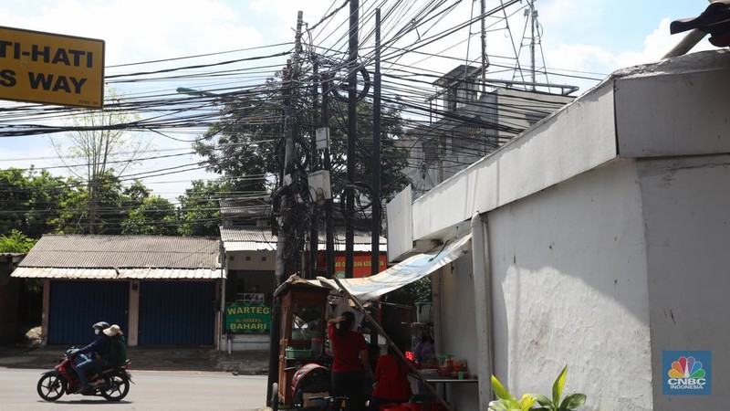 Kendaraan melintas di samping kabel yang semrawut di kawasan jalan Raya Pd. Gede, Pinang Ranti, Jakarta Timur, Jumat (3/6/2022). (CNBC Indonesia/ Andrean Kristianto)