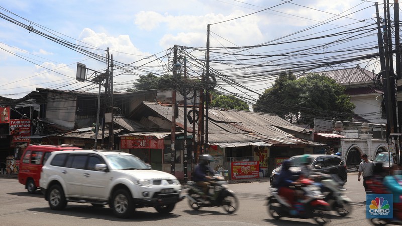 Kendaraan melintas di samping kabel yang semrawut di kawasan jalan Raya Pd. Gede, Pinang Ranti, Jakarta Timur, Jumat (3/6/2022). (CNBC Indonesia/ Andrean Kristianto)