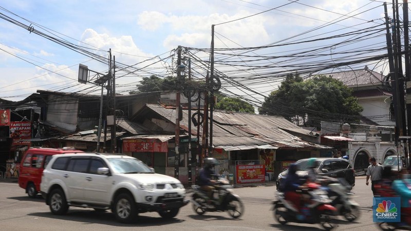 Kendaraan melintas di samping kabel yang semrawut di kawasan jalan Raya Pd. Gede, Pinang Ranti, Jakarta Timur, Jumat (3/6/2022). (CNBC Indonesia/ Andrean Kristianto)