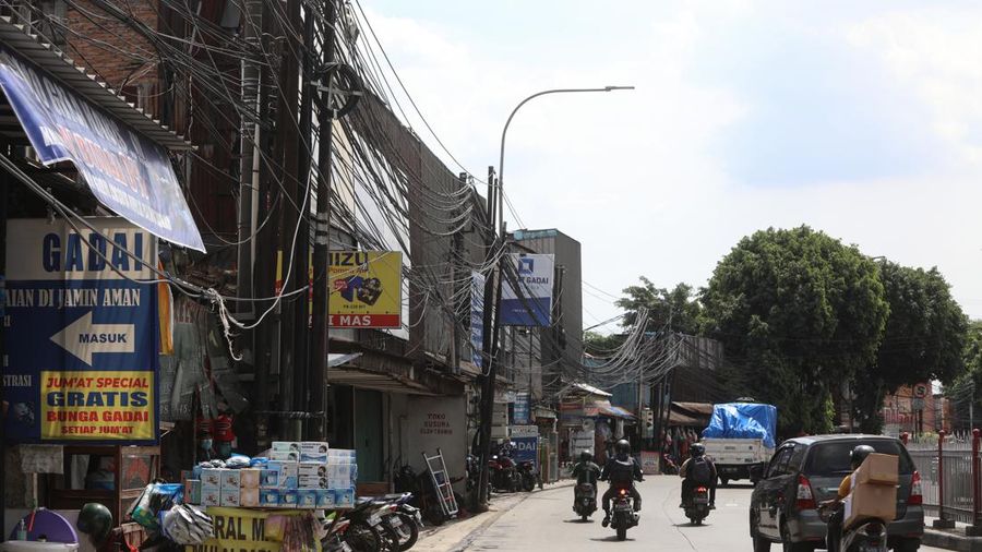 Kendaraan melintas di samping kabel yang semrawut di kawasan jalan Raya Pd. Gede, Pinang Ranti, Jakarta Timur, Jumat (3/6/2022). (CNBC Indonesia/ Andrean Kristianto)