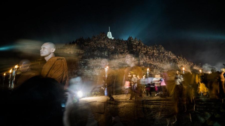 Umat Buddha berparade melewati Candi Borobudur (belakang) untuk menghormati hari lahir Buddha, juga dikenal sebagai perayaan Waisak, di Magelang, Jawa Tengah, Kamis (19/6/2022).  (Photo by OKA HAMIED / AFP)