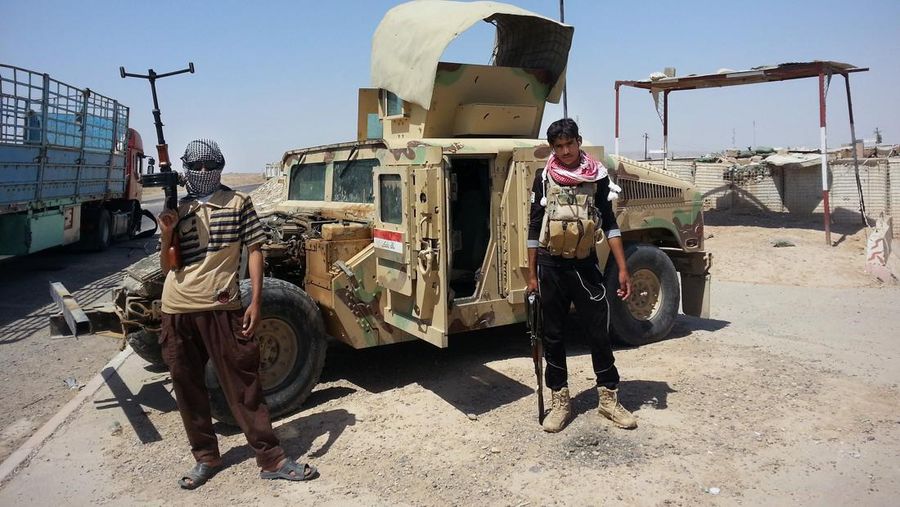 Militan yang terinspirasi al-Qaeda berdiri dengan tentara Irak yang ditangkap Humvee di sebuah pos pemeriksaan di luar kilang minyak di Beiji, sekitar 250 kilometer (155 mil) utara Baghdad, Irak. (AP/Uncredited)