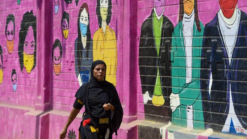 Seorang wanita berjalan melewati mural yang menggambarkan orang-orang yang mengenakan masker untuk menciptakan kesadaran tentang virus corona Covid-19 di Mumbai pada 8 Juni 2022. (AFP via Getty Images/PUNIT PARANJPE)