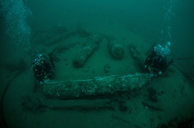 BRITAIN-SHIPWRECK/ Brothers Julian Barnwell and Lincoln Barnwell measure a cannon underwater, from the shipwreck of HMS Gloucester, which sank 340 years ago while carrying King of England, James Stuart, and was discovered off the coast of Norfolk, Britain July 25, 2018. Norfolk Historic Shipwrecks/Handout via REUTERS THIS IMAGE HAS BEEN SUPPLIED BY A THIRD PARTY. NO RESALES. NO ARCHIVES. MANDATORY CREDIT.