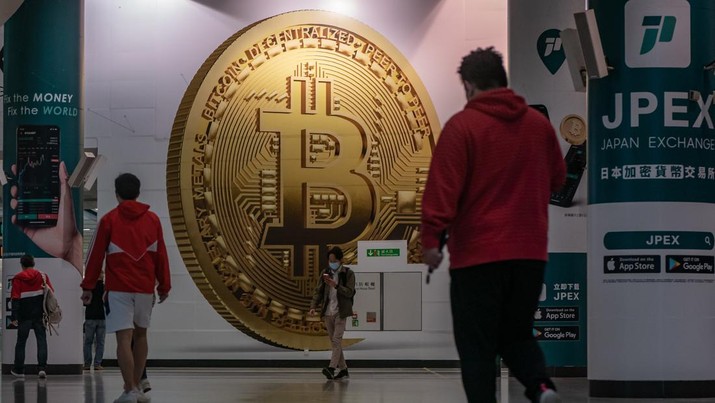Pejalan kaki melewati iklan yang menampilkan token cryptocurrency Bitcoin di Hong Kong, Selasa (15/2/2022). (Photo by Anthony Kwan/Getty Images)