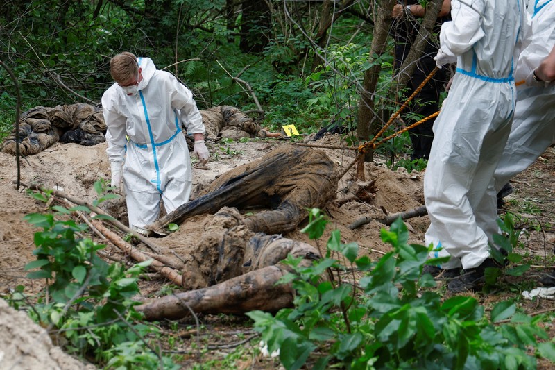 Tim forensik memasukkan ke dalam kantong jenazah tubuh seseorang yang diduga dibunuh dan dikuburkan selama serangan Rusia ke Ukraina di dekat desa Vorzel di distrik Bucha, wilayah Kyiv, Ukraina, Senin (13/6/2022). (REUTERS/Valentyn Ogirenko)