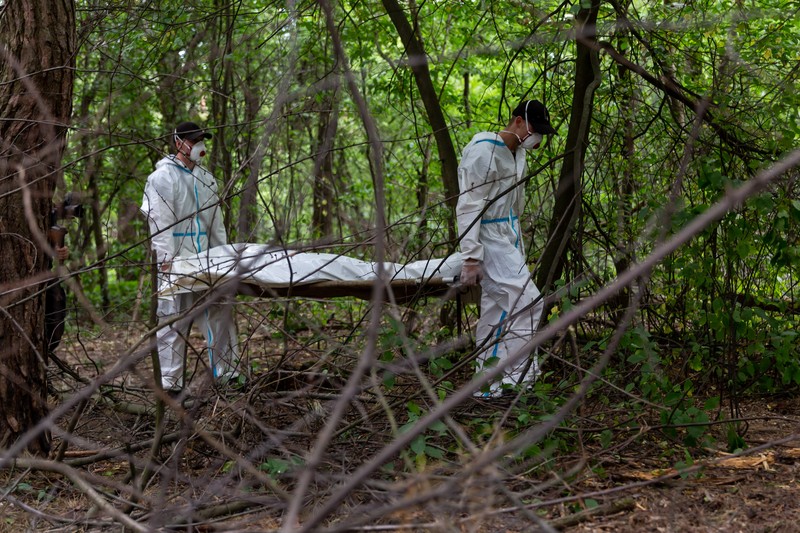 Tim forensik memasukkan ke dalam kantong jenazah tubuh seseorang yang diduga dibunuh dan dikuburkan selama serangan Rusia ke Ukraina di dekat desa Vorzel di distrik Bucha, wilayah Kyiv, Ukraina, Senin (13/6/2022). (REUTERS/Valentyn Ogirenko)