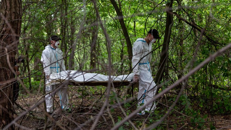 Tim forensik memasukkan ke dalam kantong jenazah tubuh seseorang yang diduga dibunuh dan dikuburkan selama serangan Rusia ke Ukraina di dekat desa Vorzel di distrik Bucha, wilayah Kyiv, Ukraina, Senin (13/6/2022). (REUTERS/Valentyn Ogirenko)