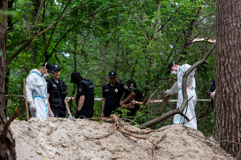 Tim forensik memasukkan ke dalam kantong jenazah tubuh seseorang yang diduga dibunuh dan dikuburkan selama serangan Rusia ke Ukraina di dekat desa Vorzel di distrik Bucha, wilayah Kyiv, Ukraina, Senin (13/6/2022). (REUTERS/Valentyn Ogirenko)