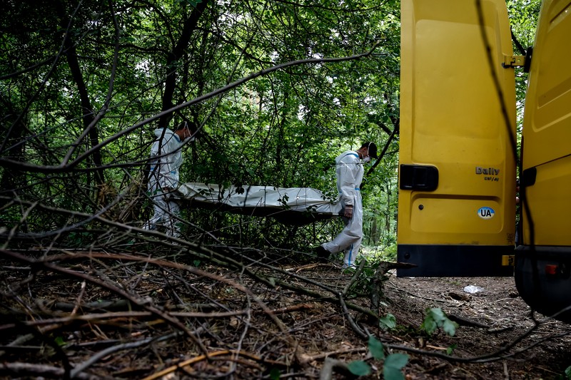 Tim forensik memasukkan ke dalam kantong jenazah tubuh seseorang yang diduga dibunuh dan dikuburkan selama serangan Rusia ke Ukraina di dekat desa Vorzel di distrik Bucha, wilayah Kyiv, Ukraina, Senin (13/6/2022). (REUTERS/Valentyn Ogirenko)
