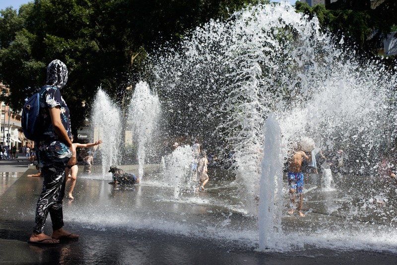 Seekor anjing berjalan melewati anak-anak yang mendinginkan diri di air mancur umum di Nice saat gelombang panas awal melanda Prancis, Rabu (15/6/2022). (REUTERS/Eric Gaillard)