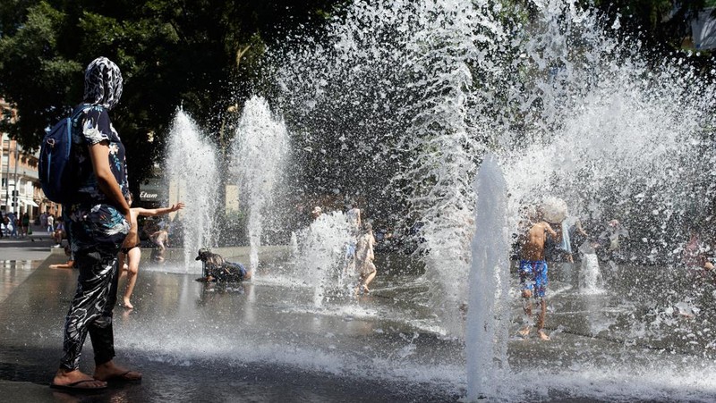 Seekor anjing berjalan melewati anak-anak yang mendinginkan diri di air mancur umum di Nice saat gelombang panas awal melanda Prancis, Rabu (15/6/2022). (REUTERS/Eric Gaillard)