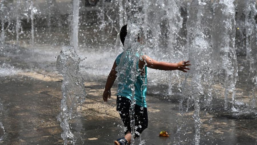 Seorang anak mendinginkan badan saat gelombang panas melanda di air mancur di pusat kota Montpellier, Prancis selatan, Selasa (14/6/2022). (Photo by PASCAL GUYOT/AFP via Getty Images)