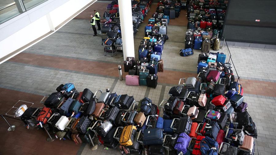 Airport workers stand next to lines of passenger luggage arranged outside Terminal 2 at Heathrow Airport in London, Britain, June 19, 2022. REUTERS/Henry Nicholls