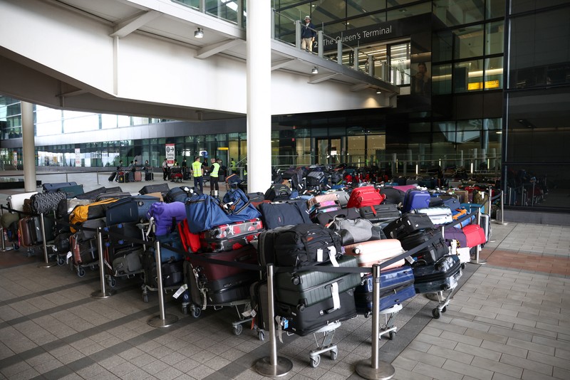 BRITAIN-AIRPORTS/ Airport workers stand next to lines of passenger luggage arranged outside Terminal 2 at Heathrow Airport in London, Britain, June 19, 2022. REUTERS/Henry Nicholls