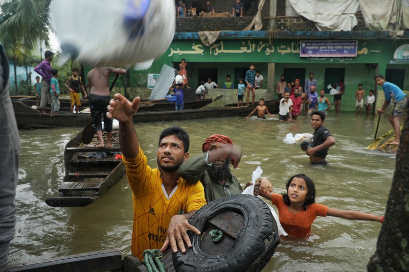 People gather to collect food aid in a flooded residential area following heavy monsoon rainfalls in Companiganj on June 20, 2022. - At least 26 more people have died in monsoon flooding and lightning strikes in India, as millions remained marooned in the country and neighbouring Bangladesh, authorities said on June 20. (Photo by Maruf RAHMAN / AFP) (Photo by MARUF RAHMAN/AFP via Getty Images)