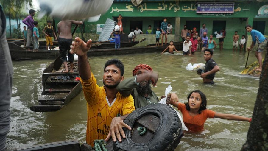 People gather to collect food aid in a flooded residential area following heavy monsoon rainfalls in Companiganj on June 20, 2022. - At least 26 more people have died in monsoon flooding and lightning strikes in India, as millions remained marooned in the country and neighbouring Bangladesh, authorities said on June 20. (Photo by Maruf RAHMAN / AFP) (Photo by MARUF RAHMAN/AFP via Getty Images)