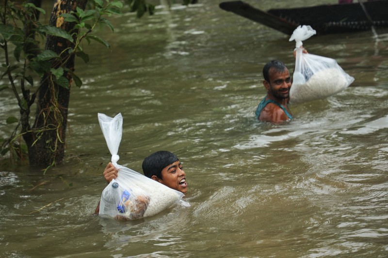 1241412249 People gather to collect food aid in a flooded residential area following heavy monsoon rainfalls in Companiganj on June 20, 2022. - At least 26 more people have died in monsoon flooding and lightning strikes in India, as millions remained marooned in the country and neighbouring Bangladesh, authorities said on June 20. (Photo by Maruf RAHMAN / AFP) (Photo by MARUF RAHMAN/AFP via Getty Images)
