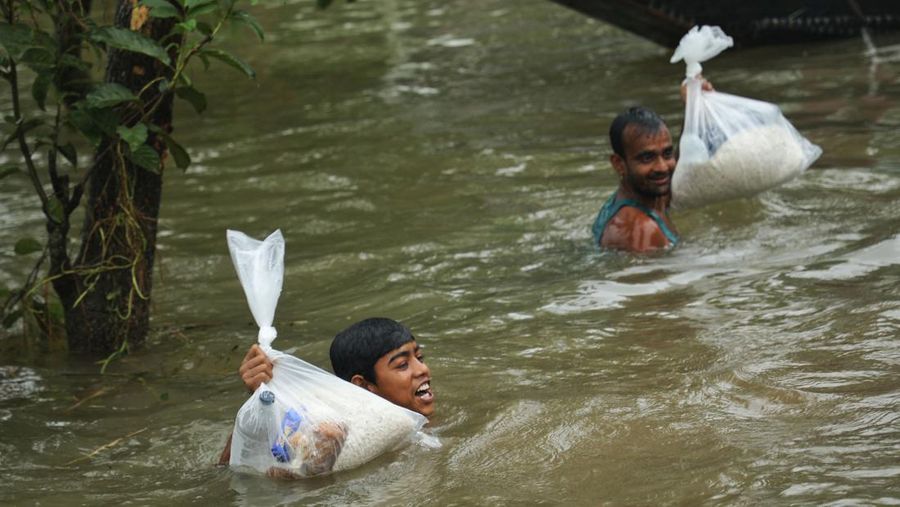 People gather to collect food aid in a flooded residential area following heavy monsoon rainfalls in Companiganj on June 20, 2022. - At least 26 more people have died in monsoon flooding and lightning strikes in India, as millions remained marooned in the country and neighbouring Bangladesh, authorities said on June 20. (Photo by Maruf RAHMAN / AFP) (Photo by MARUF RAHMAN/AFP via Getty Images)