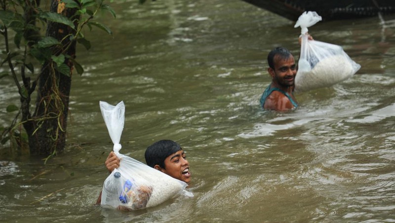 People gather to collect food aid in a flooded residential area following heavy monsoon rainfalls in Companiganj on June 20, 2022. - At least 26 more people have died in monsoon flooding and lightning strikes in India, as millions remained marooned in the country and neighbouring Bangladesh, authorities said on June 20. (Photo by Maruf RAHMAN / AFP) (Photo by MARUF RAHMAN/AFP via Getty Images)
