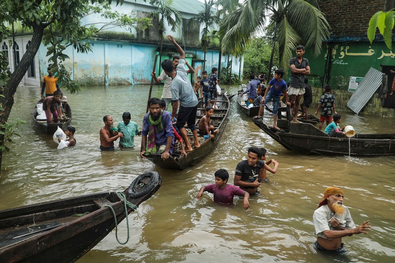 People gather to collect food aid in a flooded residential area following heavy monsoon rainfalls in Companiganj on June 20, 2022. - At least 26 more people have died in monsoon flooding and lightning strikes in India, as millions remained marooned in the country and neighbouring Bangladesh, authorities said on June 20. (Photo by Maruf RAHMAN / AFP) (Photo by MARUF RAHMAN/AFP via Getty Images)