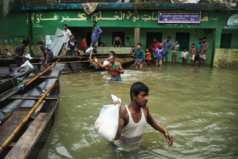 People gather to collect food aid in a flooded residential area following heavy monsoon rainfalls in Companiganj on June 20, 2022. - At least 26 more people have died in monsoon flooding and lightning strikes in India, as millions remained marooned in the country and neighbouring Bangladesh, authorities said on June 20. (Photo by Maruf RAHMAN / AFP) (Photo by MARUF RAHMAN/AFP via Getty Images)