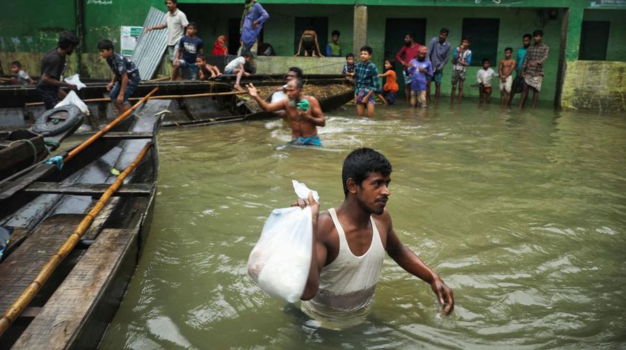 People collect food aid in a flooded residential area following heavy monsoon rainfalls in Companiganj on June 20, 2022. - At least 26 more people have died in monsoon flooding and lightning strikes in India, as millions remained marooned in the country and neighbouring Bangladesh, authorities said on June 20. (Photo by Maruf RAHMAN / AFP) (Photo by MARUF RAHMAN/AFP via Getty Images)