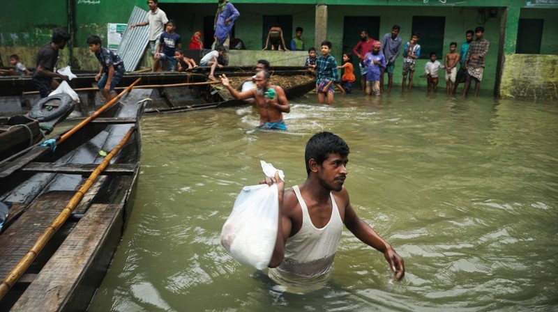 People gather to collect food aid in a flooded residential area following heavy monsoon rainfalls in Companiganj on June 20, 2022. - At least 26 more people have died in monsoon flooding and lightning strikes in India, as millions remained marooned in the country and neighbouring Bangladesh, authorities said on June 20. (Photo by Maruf RAHMAN / AFP) (Photo by MARUF RAHMAN/AFP via Getty Images)