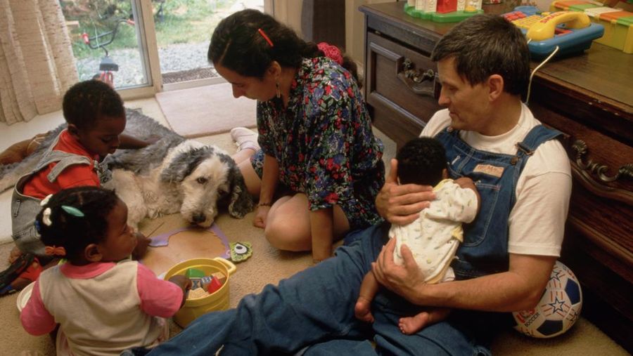 Judith and Phillip Porzel play games with their adopted son Caleb, age 3, and their foster daughter Rachel, age 16 months. Phillip cradles another foster baby in his arms.
