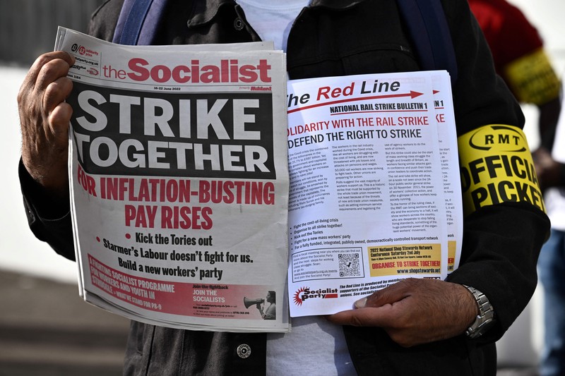 1241429779 Pamphlets and newspapers are distributed at a picket line outside Waterloo Station in London on June 21, 2022 as the biggest rail strike in over 30 years hits the UK. - Rush-hour commuters in the UK faced chaos as railway workers began the network's biggest strike action in more than three decades, with a cost-of-living crisis threatening wider industrial action. (Photo by Ben Stansall / AFP) (Photo by BEN STANSALL/AFP via Getty Images)
