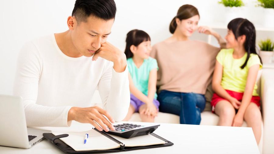 stress man calculating bills while family sitting on the sofa