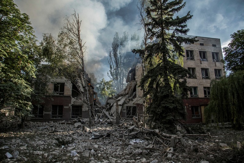 Seorang wanita berjalan melewati kawah cangkang di depan bangunan tempat tinggal yang rusak di kota Siversk, wilayah Donetsk. (AFP via Getty Images/ANATOLII STEPANOV)
